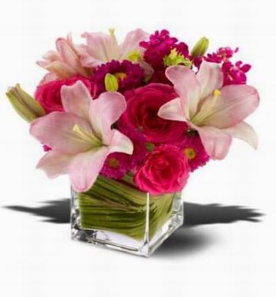 Hot pink roses pale pink lilies and mixed blossoms arranged in a modern glass cube vase.