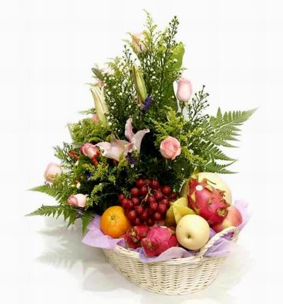 Flower basket of 8 pink roses, 3 open pink Lily buds surrounded by green leaves and fillers with Globe Grapes, 1 Orange, 3 Dragon Fruits, 1 Star Fruit, 1 yellow Fuji Apple, 1 Peach and 1 Cantaloupe.