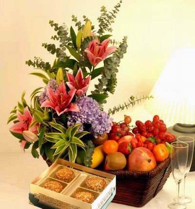 A box of Standard Mooncakes and a Flower basket of 6 pink Gerbera Daisies, 4 Lily buds, Orchids and fillers with Globe Grapes, 1 Cantaloupe, 2 red Apples, 2 green Apples, 4 Plums, 2 Kiwis, 3 Oranges, 2 Fuji Apple, 2 Dragon Fruits and 1 Mango. Basket may v