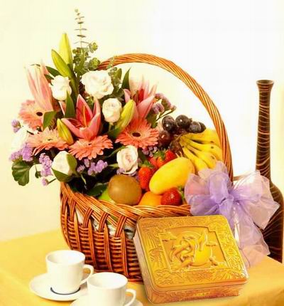 A box of Premium Mooncakes and a Fruit and Flower basket of 3 Lilies 6 light pink Roses, 4 pink Gerbera Daisies, purple Stock and Greenery with 6 Strawberries, 5 Bananas, 1 Mango, 1 Orange, 1 Kiwi, 1 green Apple, and purple Grapes.