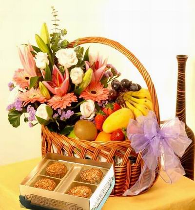 A box of Standard Mooncakes and a Fruit and Flower basket of 3 Lilies 6 light pink Roses, 4 pink Gerbera Daisies, purple Stock and Greenery with 6 Strawberries, 5 Bananas, 1 Mango, 1 Orange, 1 Kiwi, 1 green Apple, and purple Grapes.